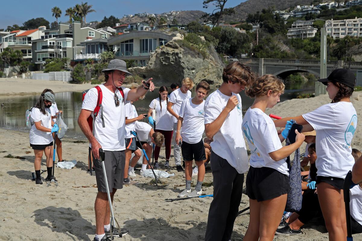 David Brobeck, left, FLOW program coordinator, directs 26 students to remove trash and plastic pollution at Aliso Beach.