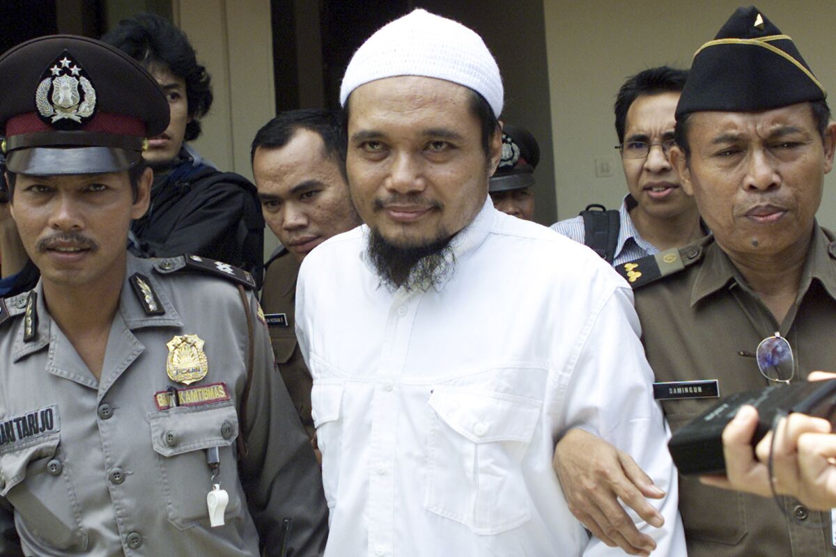 FILE - Militant cleric Abu Rusdan, center, is escorted by security officers after his trial hearing at a district court in Jakarta, Indonesia, in this Monday, Nov. 3, 2003 file photo. Indonesia's elite counterterrorism squad has arrested the convicted militant and suspected leader of an al-Qaida-linked group that has been blamed for a string of past bombings in the country, Indonesia police said Monday, Sept. 13, 2021. (AP Photo/Tatan Syuflana, File)