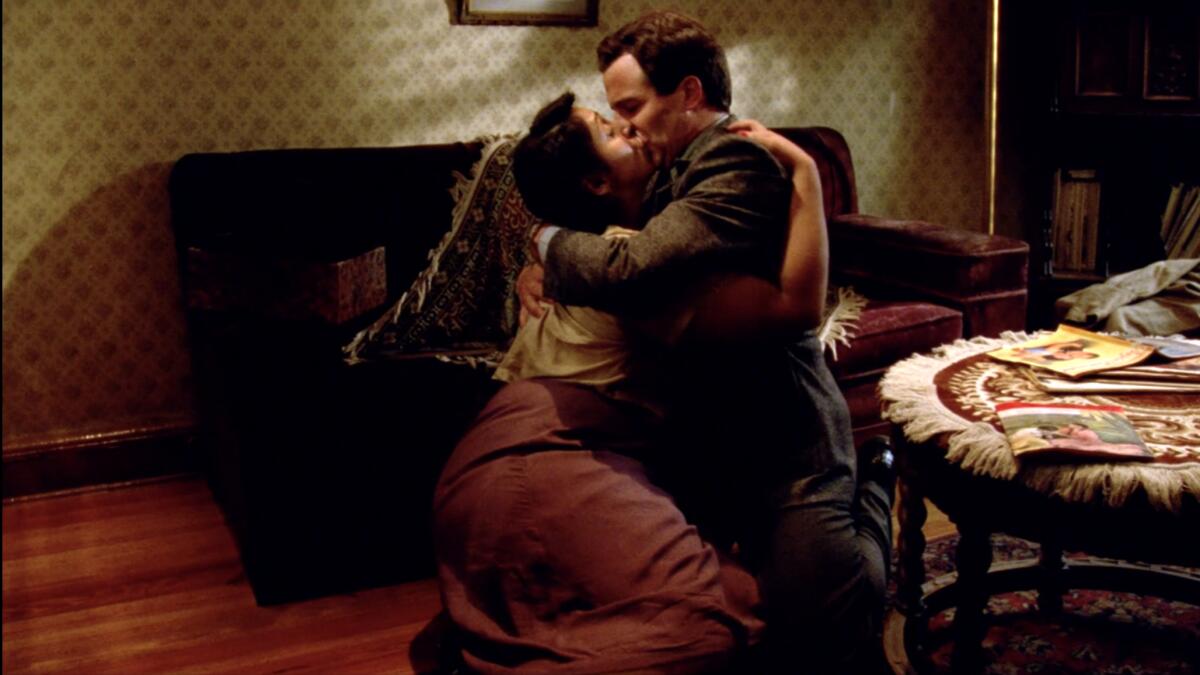 A man and a woman kiss on the floor of a living room.