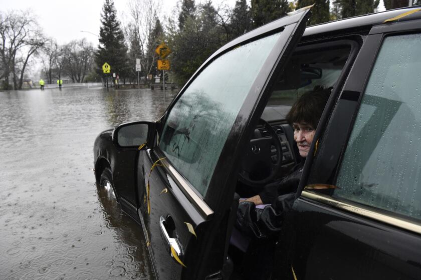 An elderly woman peeks from an open door of her car, which is sitting in a flooded area.