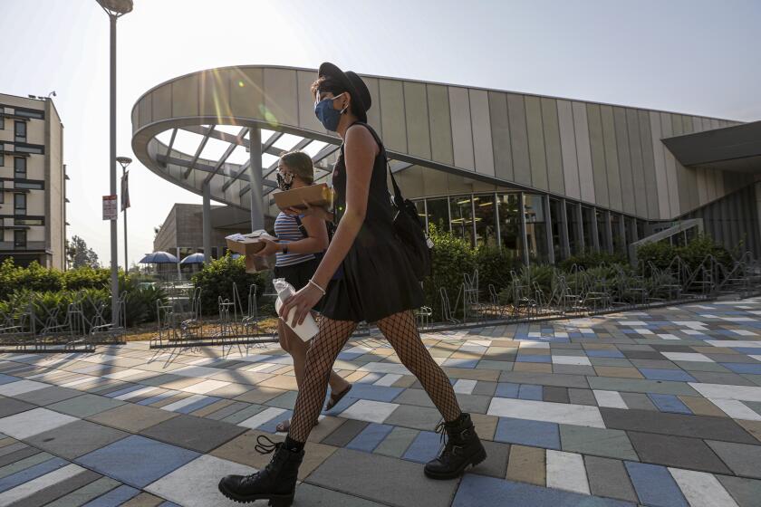 FULLERTON, CA - AUGUST 21: Madison Dabalos, 18, left, and Ixchel Cisneros, 18, wearing face masks walk back to their dorms takeout breakfast from Gastronome at Cal State University of Fullerton on Friday, Aug. 21, 2020 in Fullerton, CA. (Irfan Khan / Los Angeles Times)