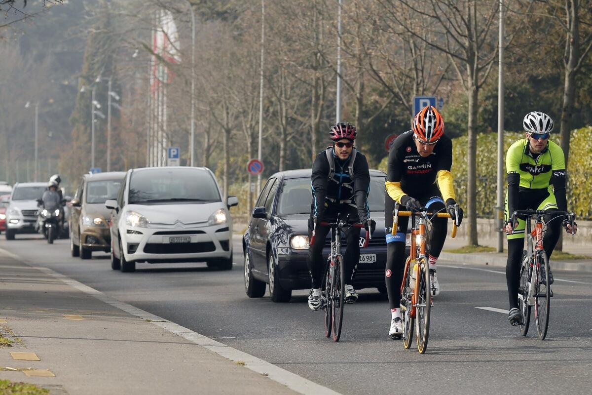 Secretary of State John Kerry, center, flanked by security guards, rides his bicycle along the shore of Lake Geneva, after holding meetings with Iran's Foreign Minister Javad Zarif over Iran's nuclear program, in Lausanne, Switzerland, Monday.