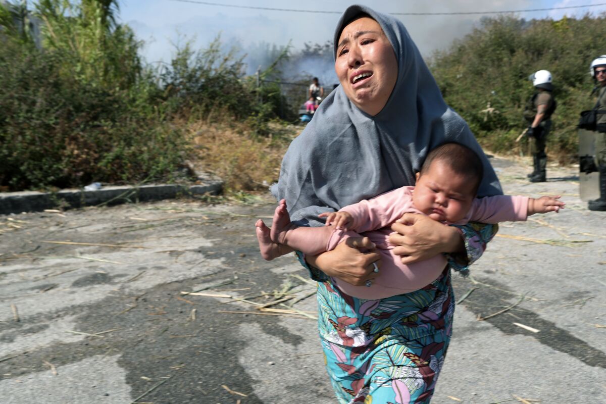 A migrant holds her baby as she runs to avoid a small fire in a field near Mytilene town, on Greece.