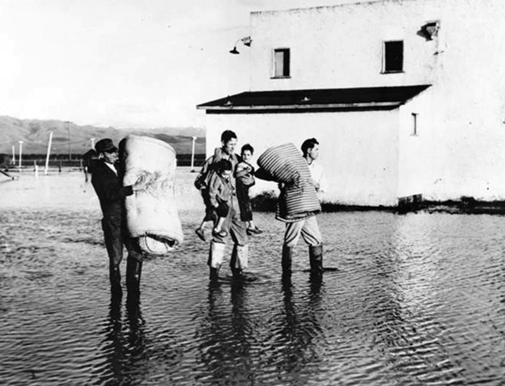 Three people and two children wade through floodwaters.