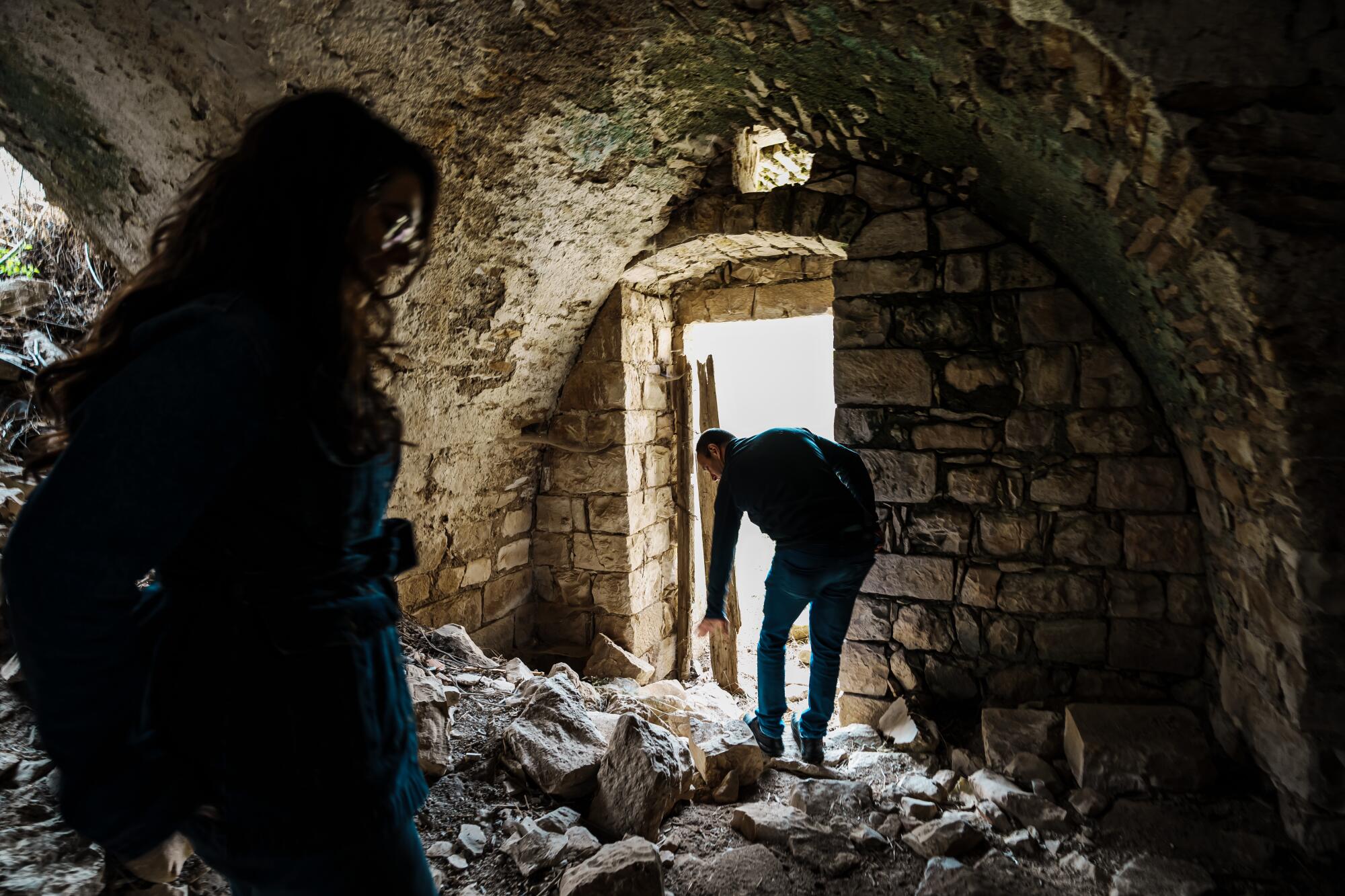 A woman, left, and a man inside a rubble-strewn home with brick walls 