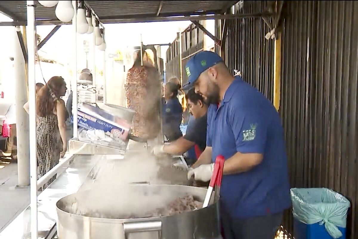 Workers on a flat-top grill at a sidewalk taco stand