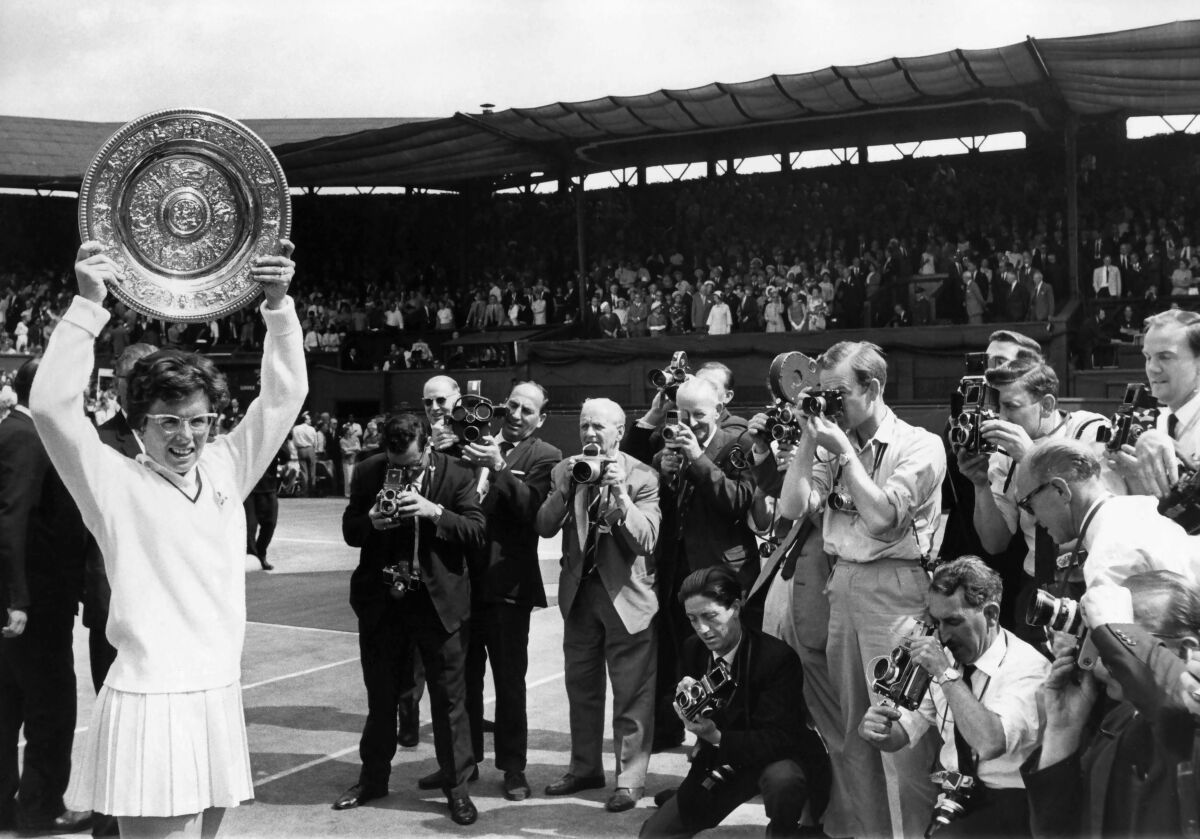 Billie Jean King hoists the Venus Rosewater Dish, her first Wimbledon singles win in 1966, for a crowd of photographers.