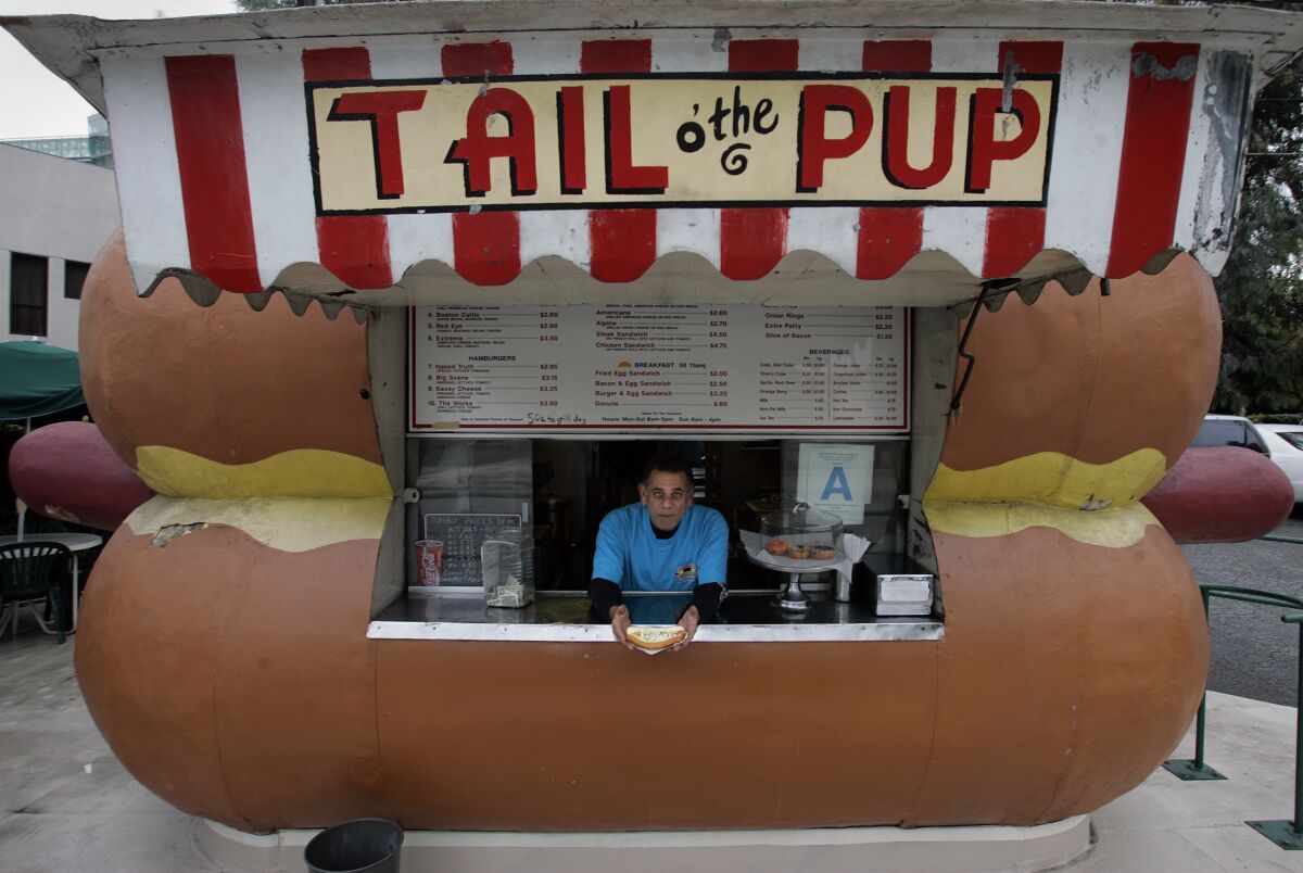 A man peeks out the service window of a hot-dog-shaped food stand.