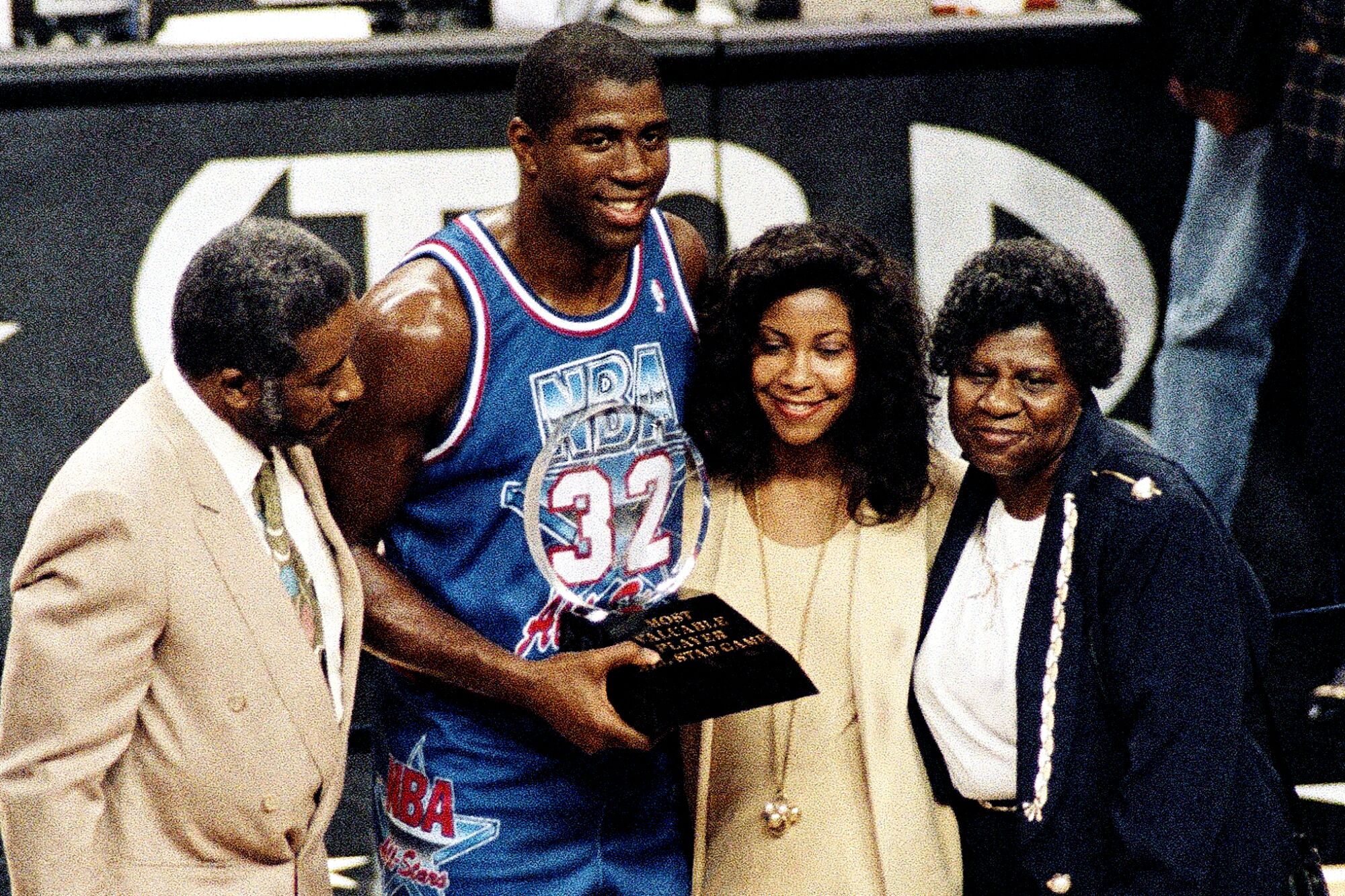 Magic Johnson poses holding All-Star game MVP trophy with his parents and wife, Cookie