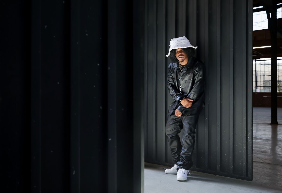 homme portant un chapeau de seau blanc debout tout en noir contre un mur noir