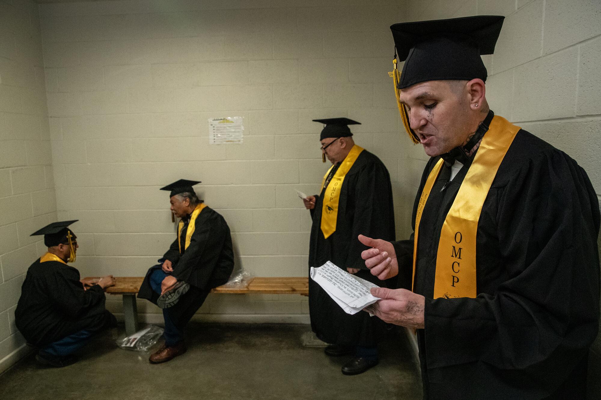 Four men in cap, gown and yellow sashes practice speeches 