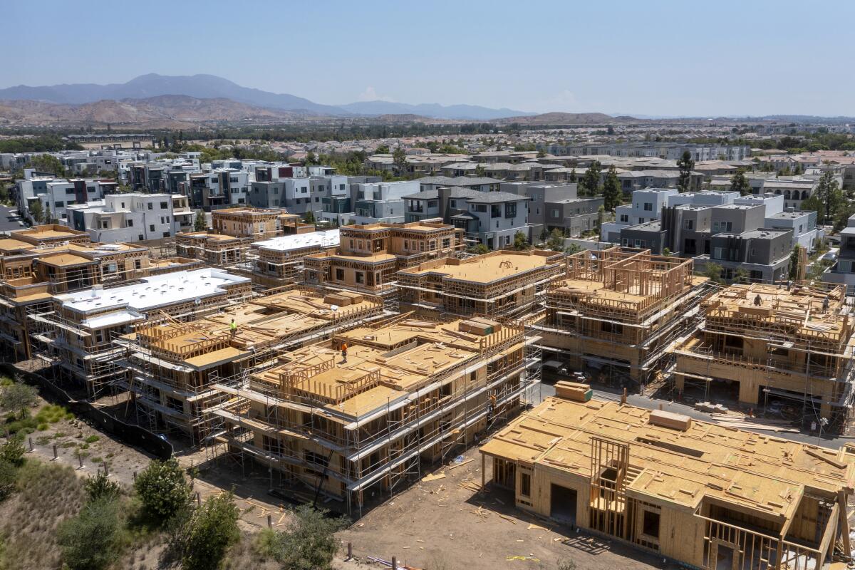 An aerial view of two diagonal rows of homes under construction with finished townhouses behind them. 