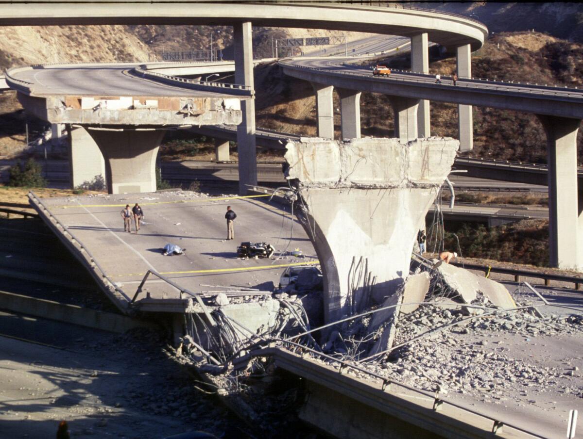 A body lies near a motorcycle on a fallen span of a collapsed freeway interchange.
