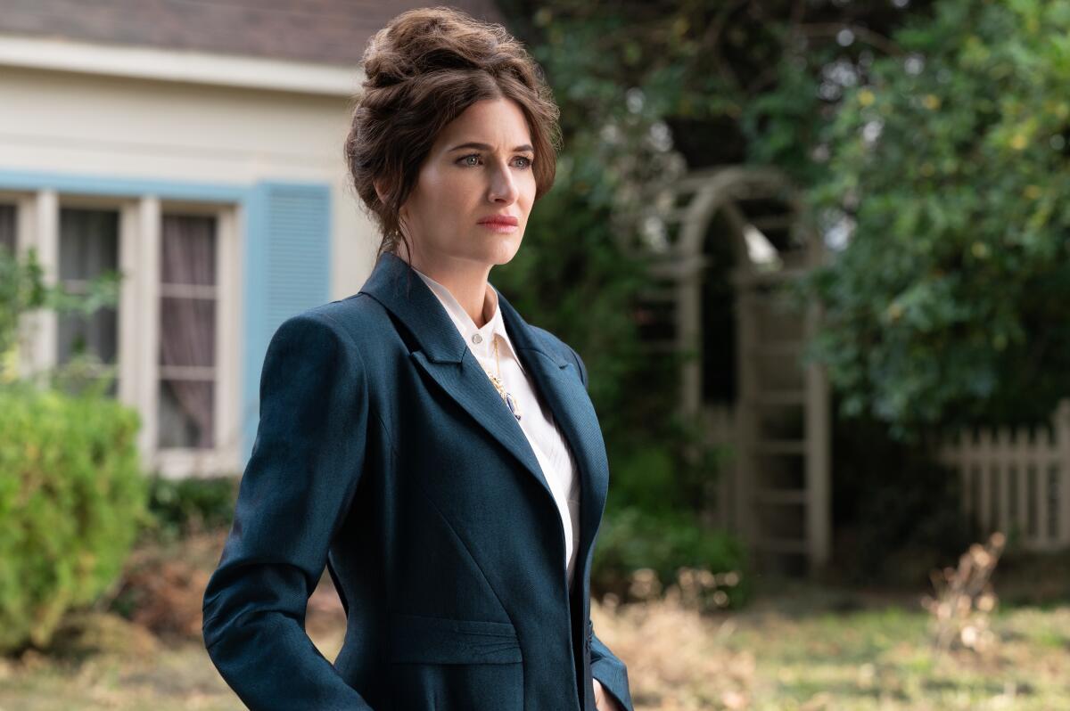 Kathryn Hahn, in a blue blazer, stands in front of a suburban home in "Agatha All Along."