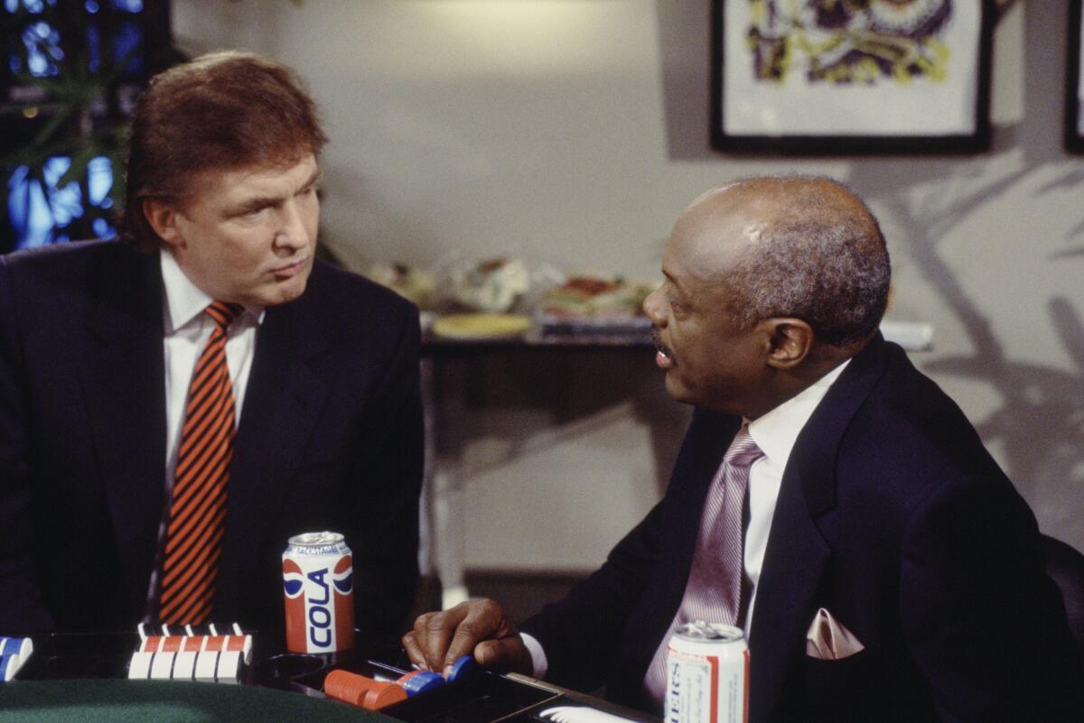 Donald Trump in dark suit and striped tie and Willie Brown in dark suit and dark pink tie sit at a games table.