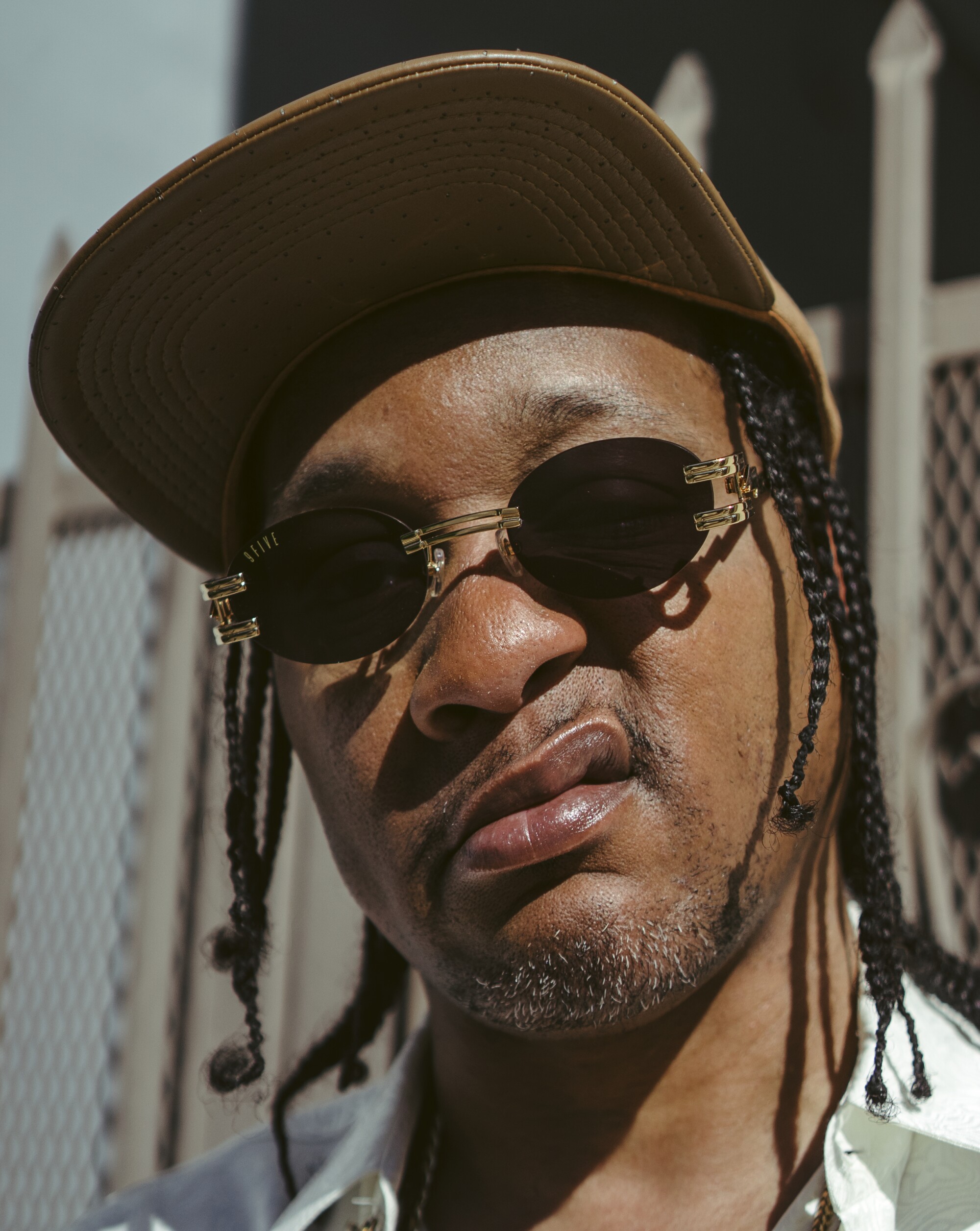 DJ Quik, wearing a hat and sunglasses, makes a face for the camera.