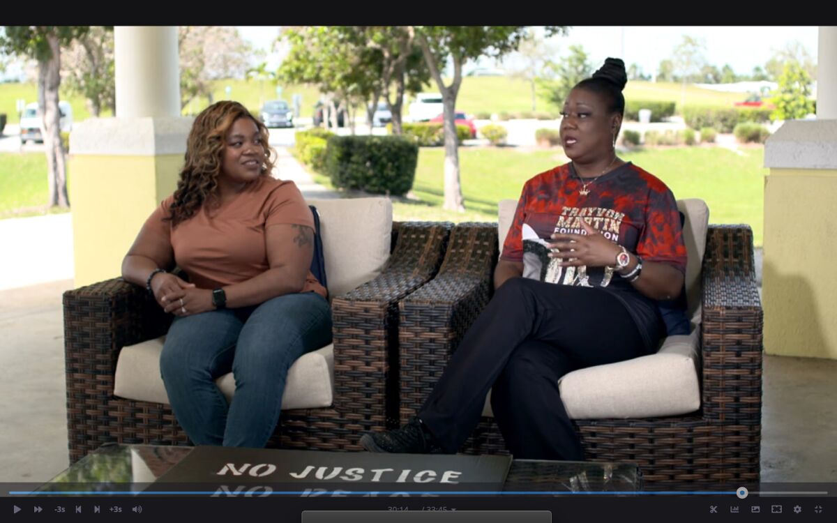 Two women on outdoor patio chairs, the one on the right wearing a shirt saying "Trayvon Martin Foundation."