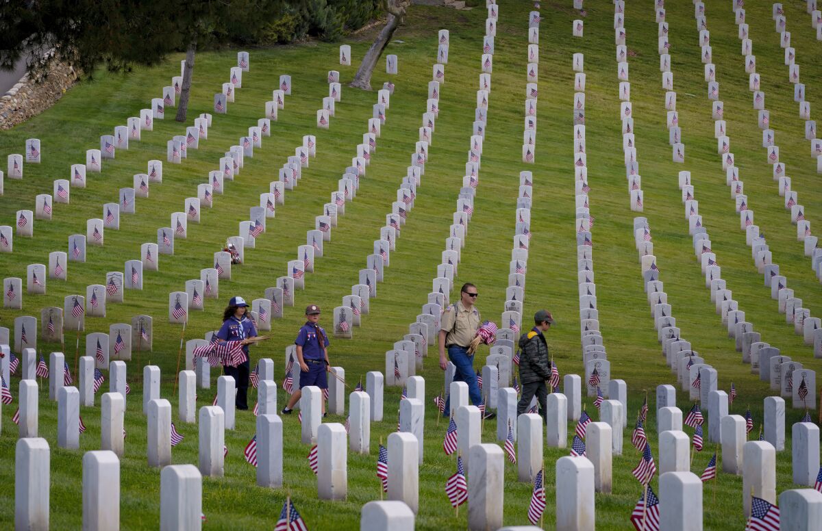 A small Scout group walks with flags among the headstones