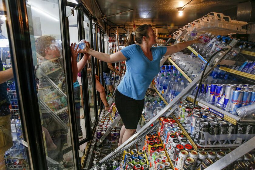 Helen McDonald and her sons help remove drink bottles from toppled shelving in coolers at Minit Shop in Ridgecrest after a 6.4 earthquake Thursday morning.