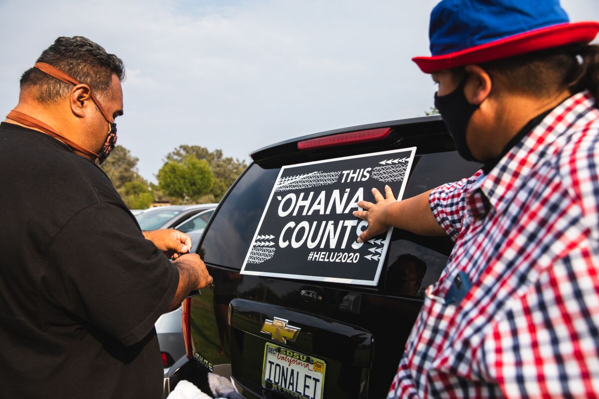 Tana Lepule and Eddie Paje put posters on an SUV to encourage participation in the census.