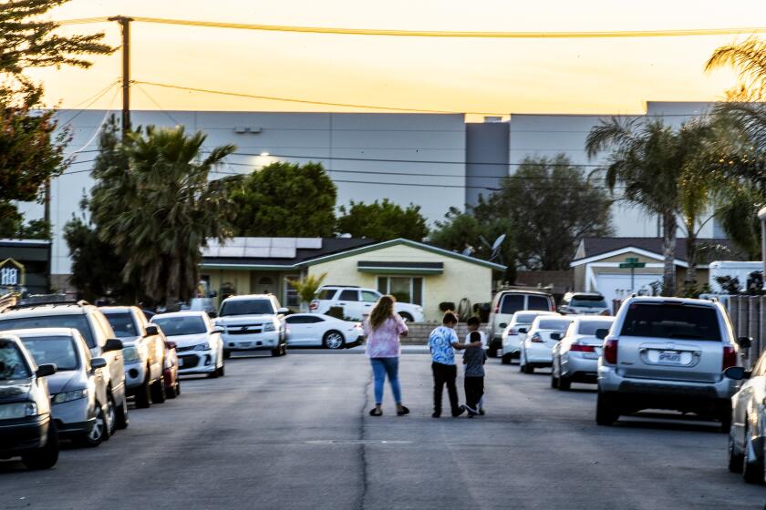JURUPA VALLEY, CA - APRIL 30, 2021: A family walks in their neighborhood which is surrounded on two sides by giant warehouses off Etiwanda Avenue on April 30, 2021 in Jurupa Valley, California. The increase in warehouses in the Inland Empire has also increased the diesel truck traffic causing more air pollution in the Southland.(Gina Ferazzi / Los Angeles Times)