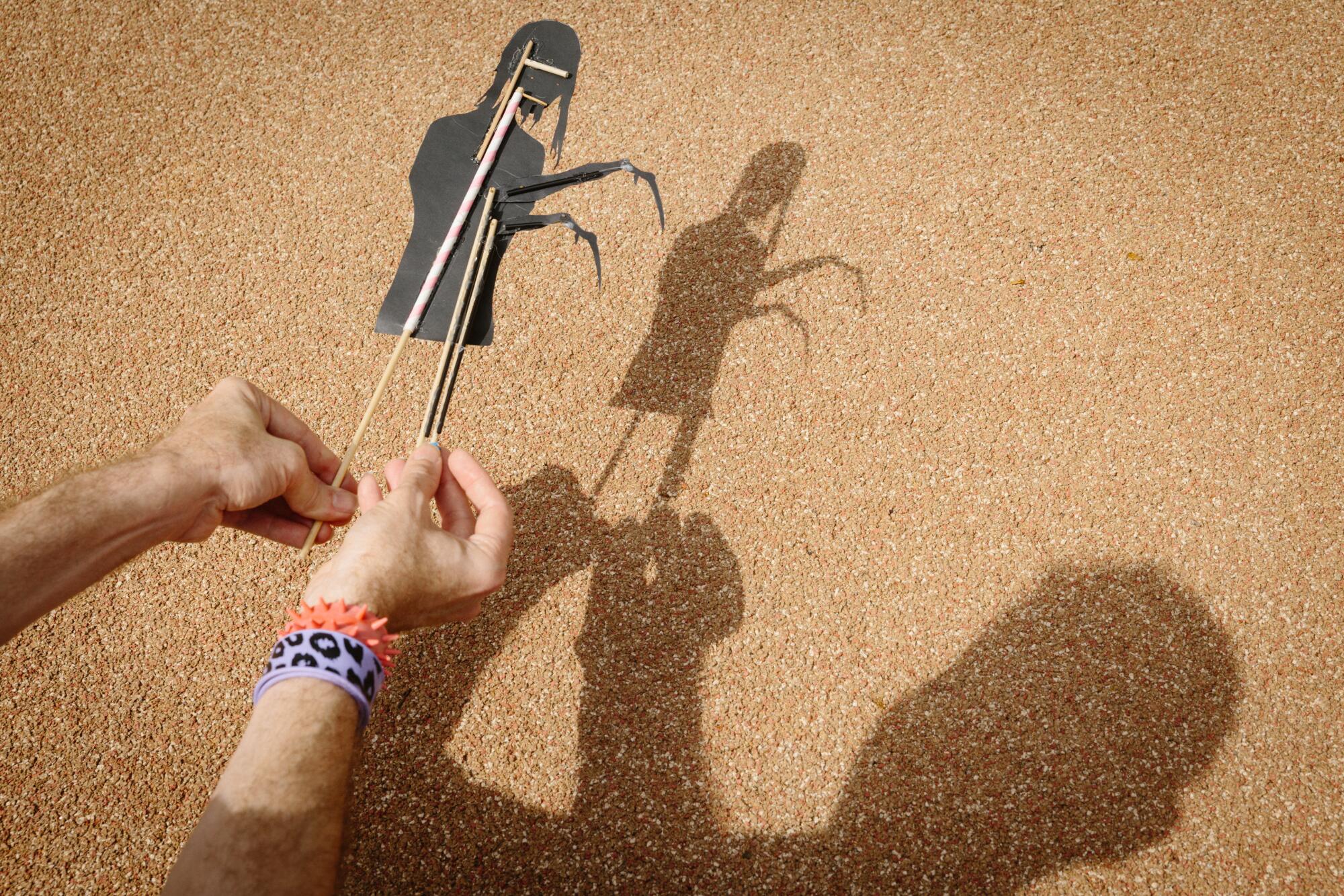 A shadow puppet is manipulated, with its shadow in the background.