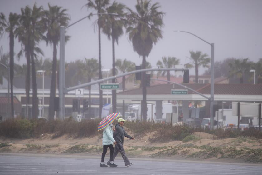 Huntington Beach, CA - March 15: A walk with an umbrella amidst the rain at Bolsa Chica State Beach, which is partially closed after both sides of PCH were closed due to flooding between Warner Avenue and Seapoint Street in Huntington Beach Wednesday, March 15, 2023. Re-opening times were not announced. (Allen J. Schaben / Los Angeles Times)