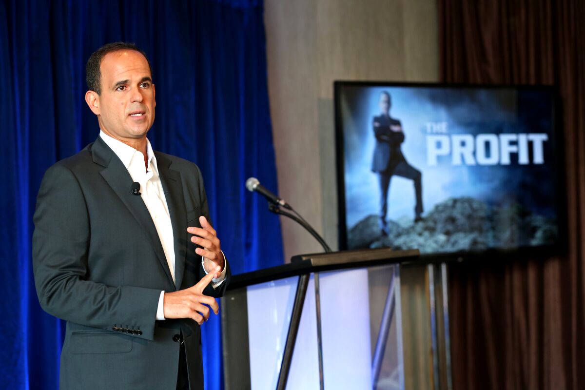 Marcus Lemonis stands beside a monitor showing the "The Profit" logo.
