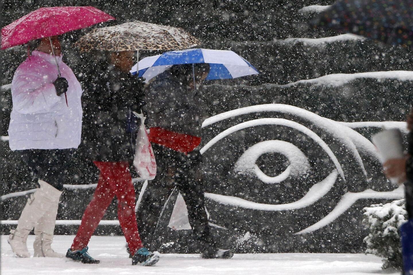 A group walks past a sculpture in downtown Pittsburgh as snow starts to fall.