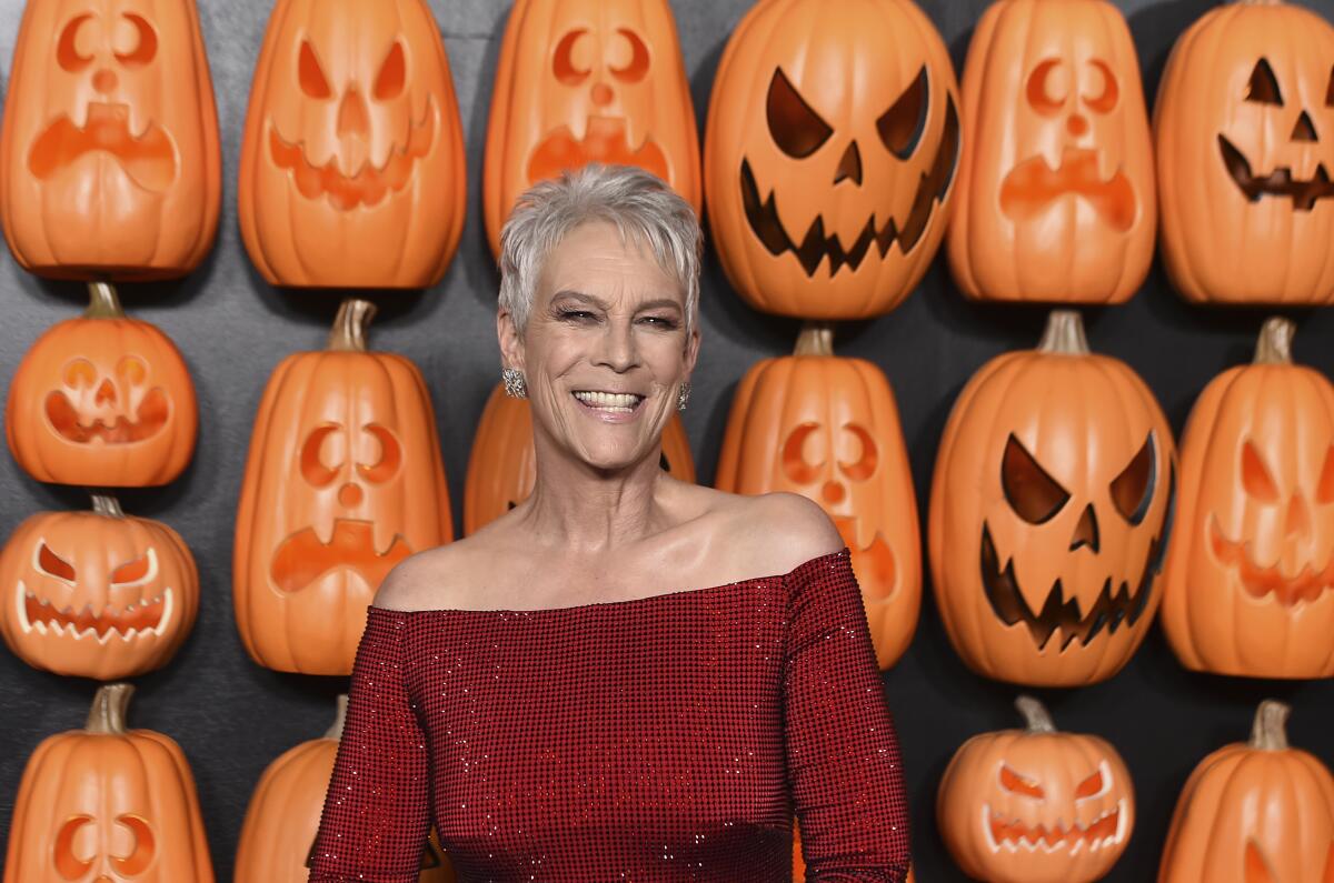 A woman in a red dress with a white hair in a pixie cut poses for pictures in front of a wall of jack-o-lanterns