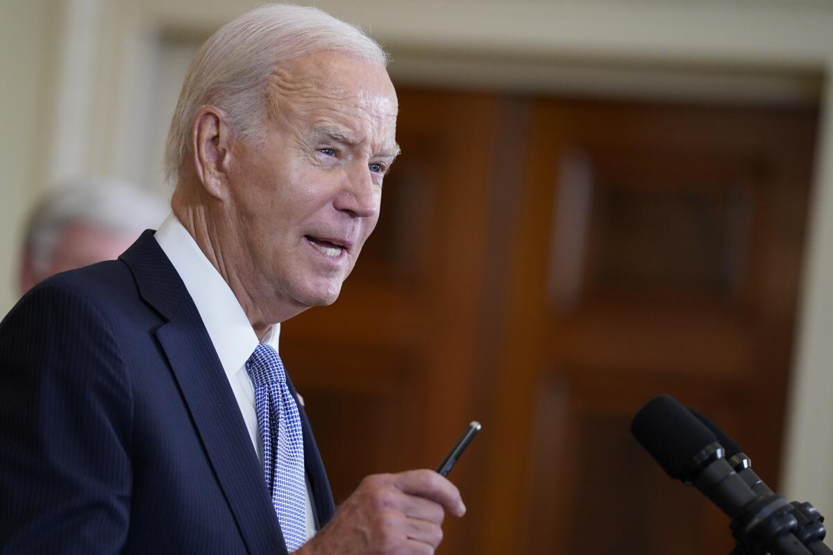 Joe Biden holds a pen while speaking at a lectern.