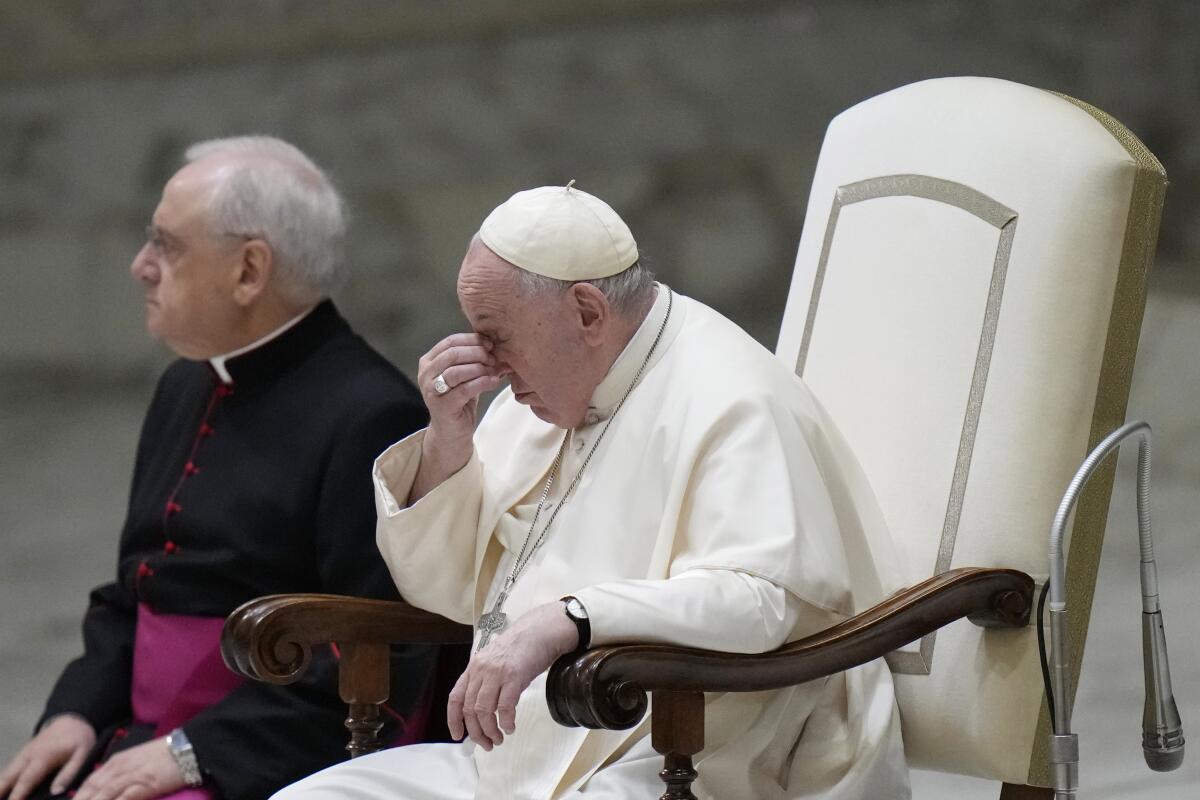 Pope Francis touches the bridge of his nose as he sits next to Monsignor Leonardo Sapienza
