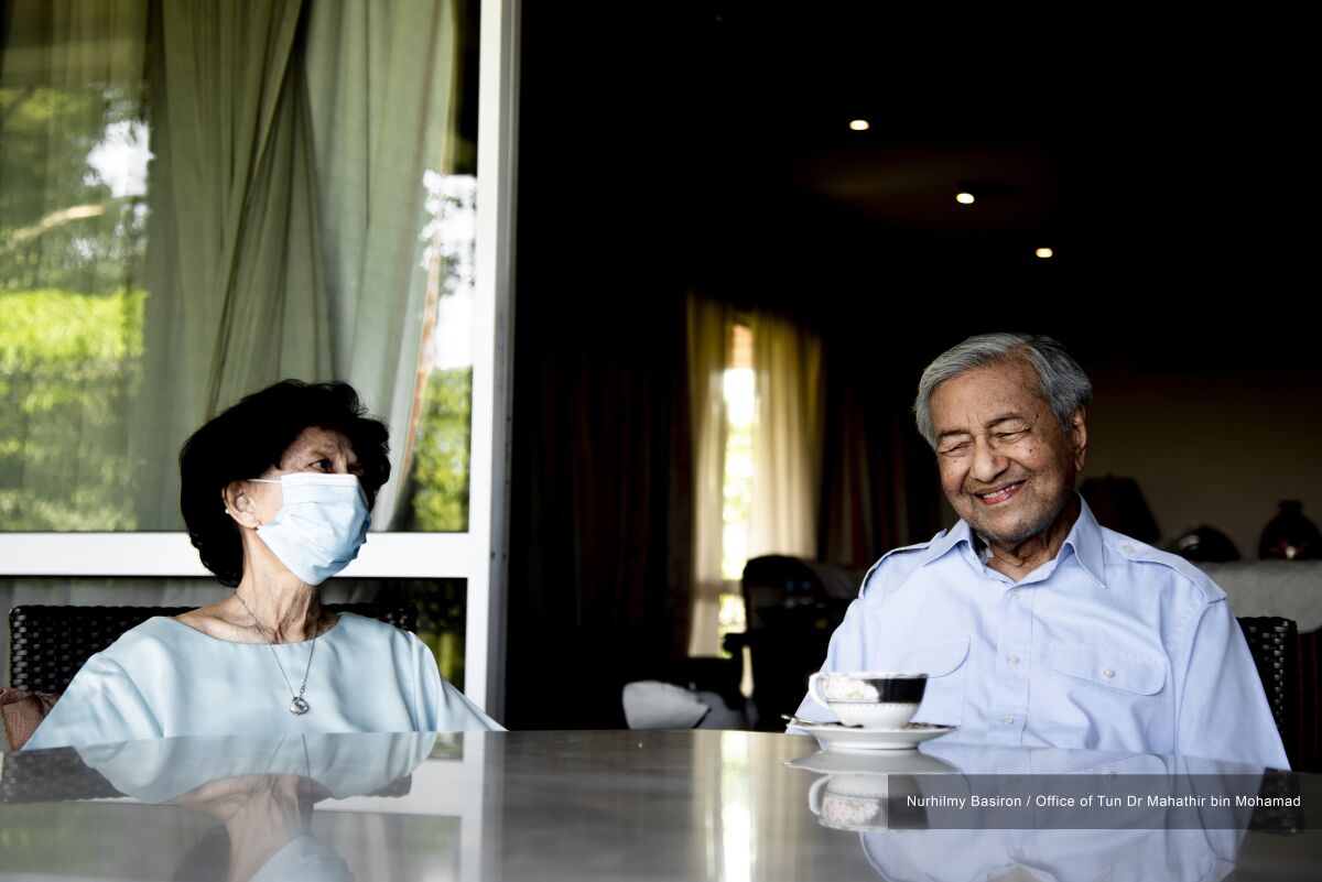 In this photo provided by the Office of Mahathir bin Mohamad, former Malaysian Prime Minister Mahathir Mohamad poses for a photo with his wife Siti Hasmah Mohamad Ali at their home in Kuala Lumpur, Malaysia, Friday, Feb. 4, 2022. Mahathir Mohamad was discharged Saturday from the National Heart Institute two weeks after he was admitted and will recuperate at home, the hospital said. (Nurhilmy Basiron/Office of Mahathir bin Mohamad via AP)