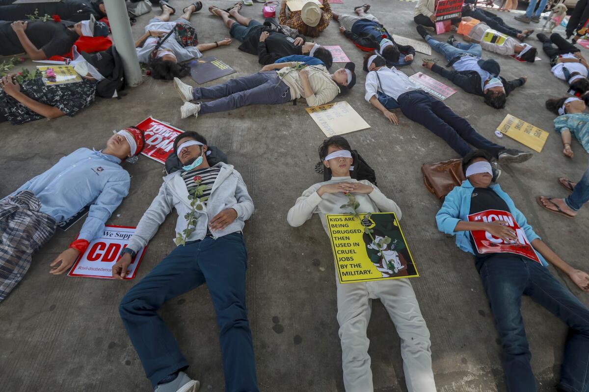 Blindfolded people with signs lie on a street in Myanmar.