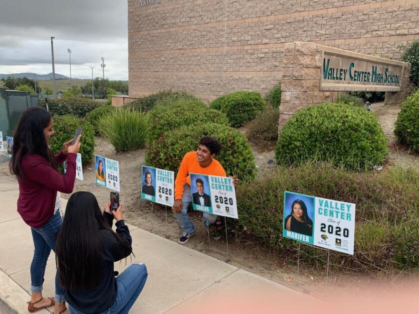 Graduating Valley Center High School senior Carlos Genis smiles as his sister, Kaylee Genis, right, and their mom, Edith Segura, take pictures at his photo sign.