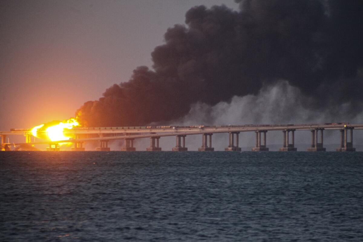 A burning bridge seen at a distance over a body of water 