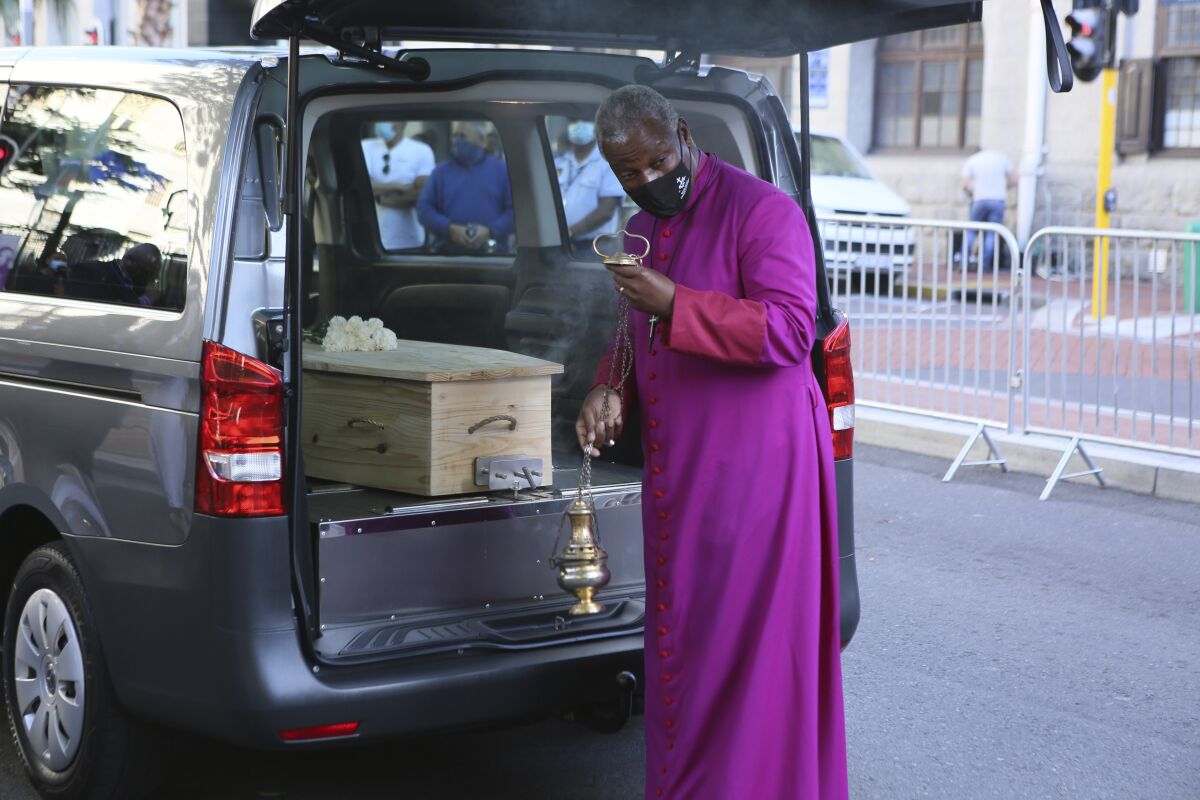 Cleric in purple robe next to vehicle carrying Desmond Tutu's coffin