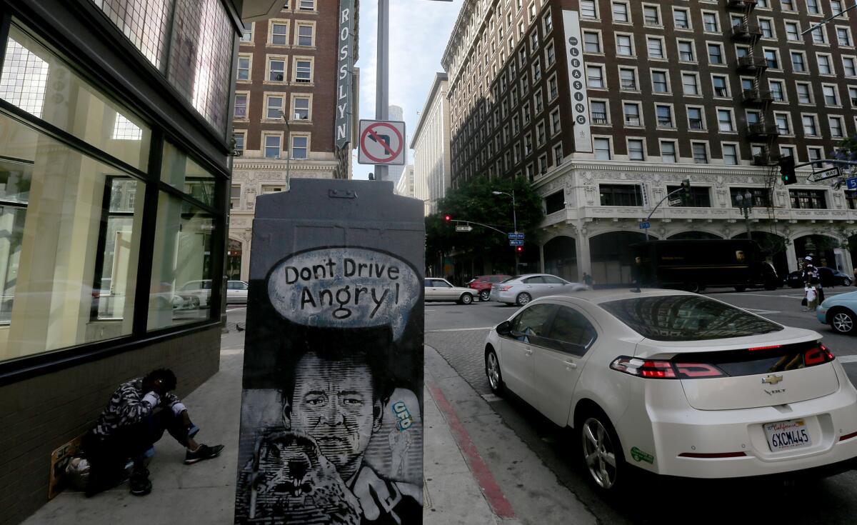 A man sits on the sidewalk at the corner of 5th and Main Streets in a downtown area known as "the corridor."