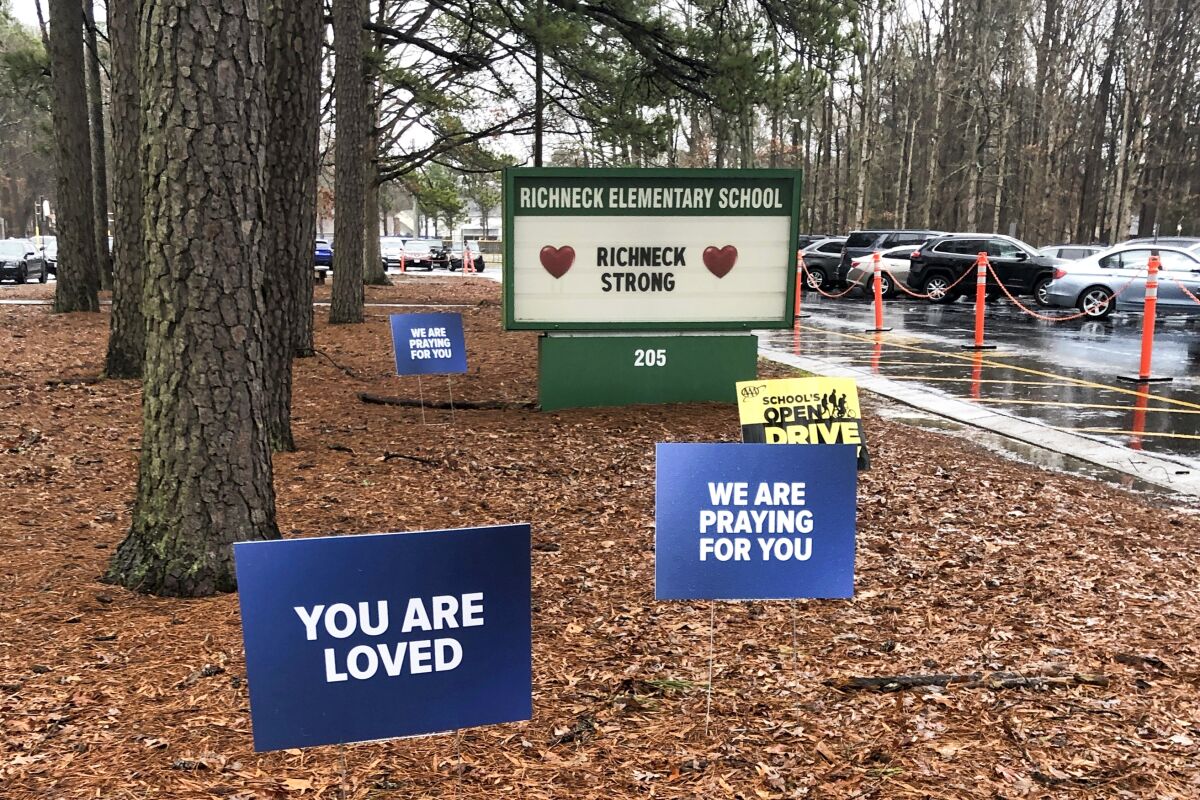 Blue signs on the ground near trees outside Richneck Elementary School say "You Are Loved" and "We Are Praying for You."