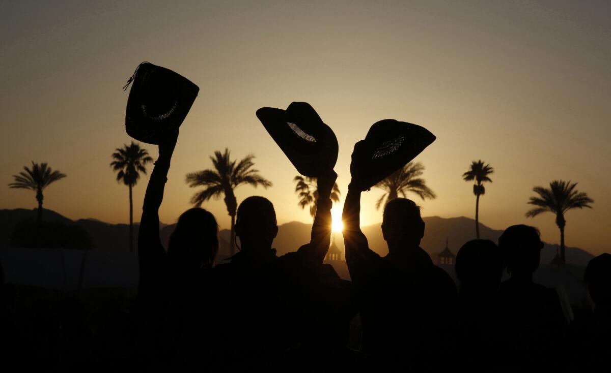 Fans are silhouetted at sunset as they cheer for Dwight Yoakam's performance on the Palomino Stage.