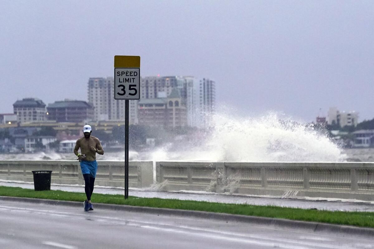 A jogger makes his way along Bayshore Blvd., in Tampa, Fla. as a wave breaks over a seawall, during the aftermath of Tropical Storm Elsa Wednesday, July 7, 2021. The Tampa Bay area was spared major damage as Elsa stayed off shore as it passed by. (AP Photo/John Raoux)