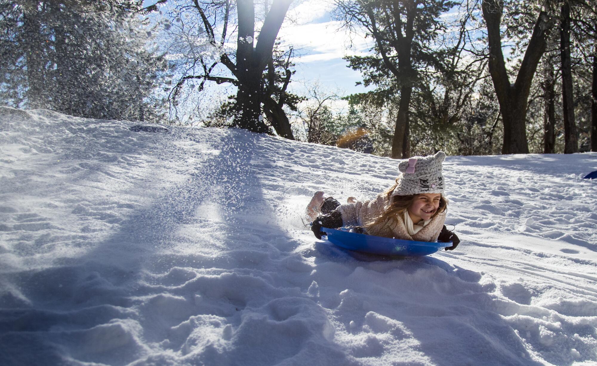 A girl smiles as she slides down a snowy slope