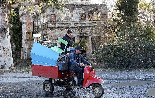 Two men carrying school chairs and desks on a motorized vehicle pass the shell of a building on the outskirts of Sukhumi, the capital city of the self-proclaimed, but universally unrecognized, republic of Abkhazia. The region along the Black Sea fought a separatist war with Georgia in the early 1990s. The Russian parliament is pushing to beef up the number of Russian peacekeepers stationed in Abkhazia, and has suggested that Moscow might fight on the side of the breakaway republic in case of any military aggression from Georgia, whose push to join the North Atlantic Treaty Organization is backed by the U.S.