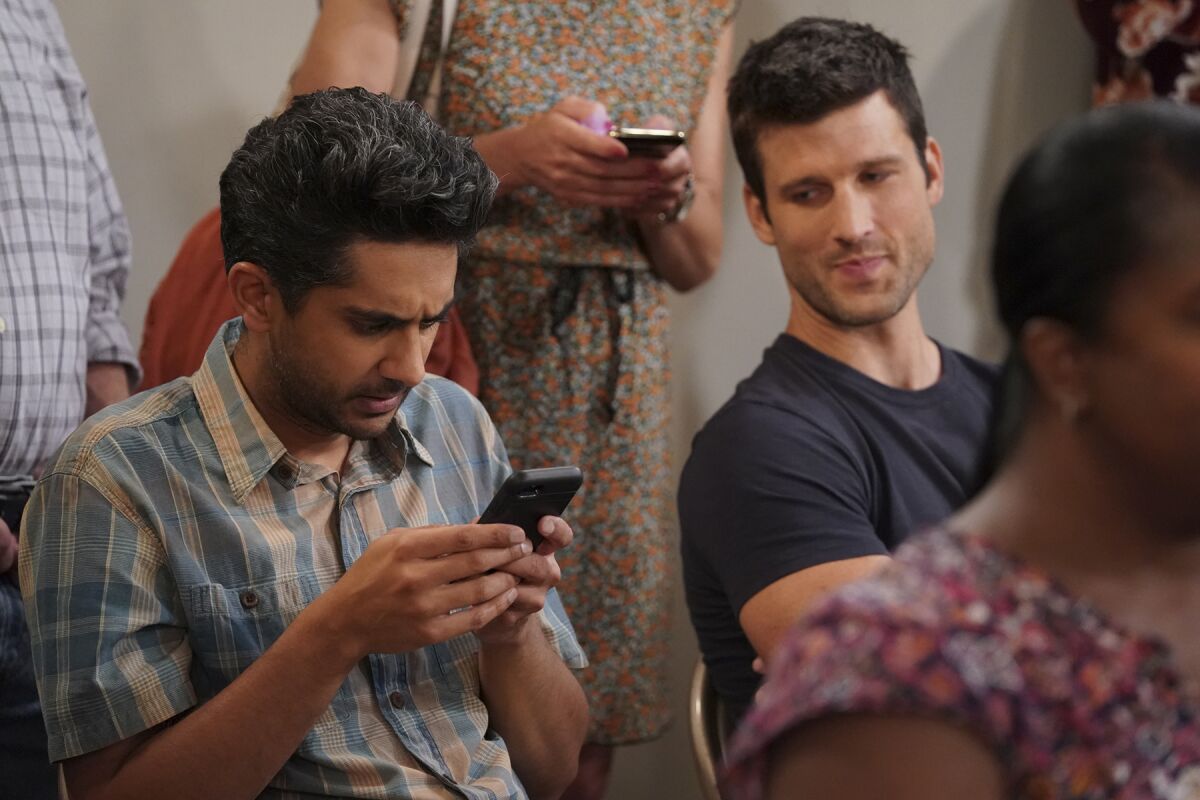 Two young men seated, one staring unhappily at his cellphone.