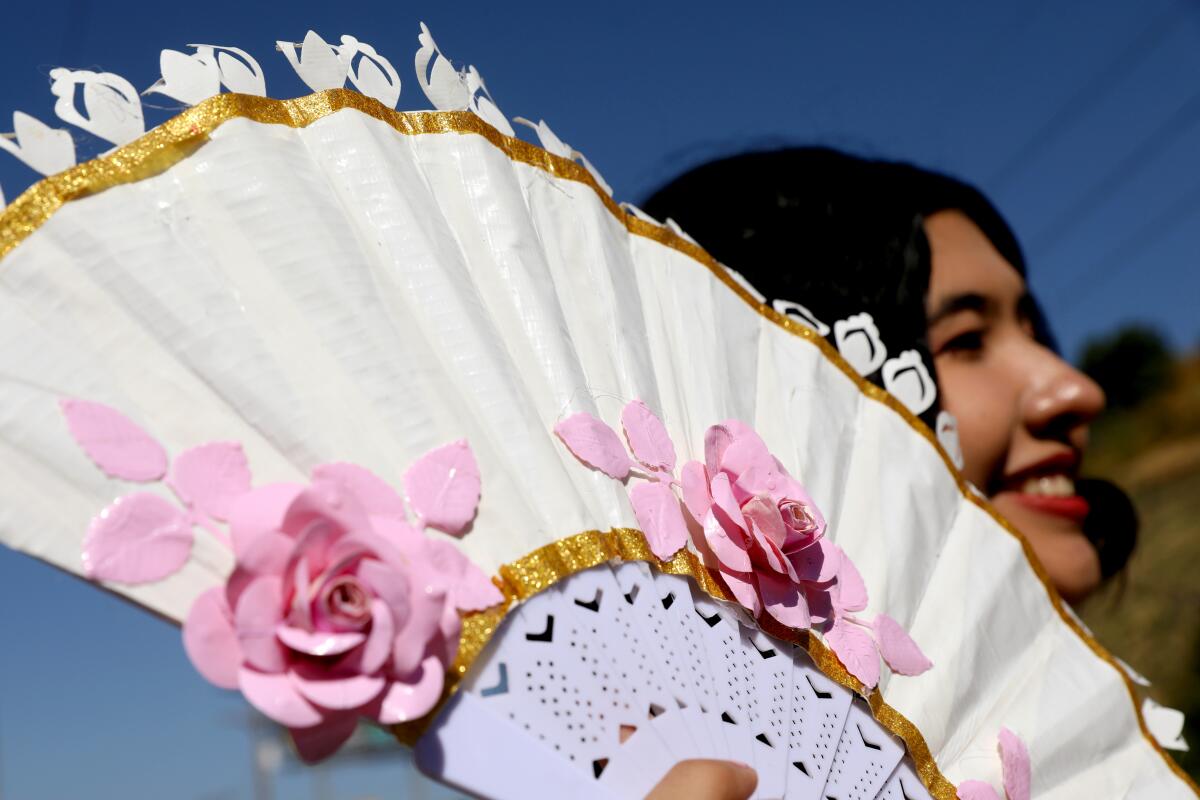 A close up detail of a young woman holding up a white fan with pink roses.