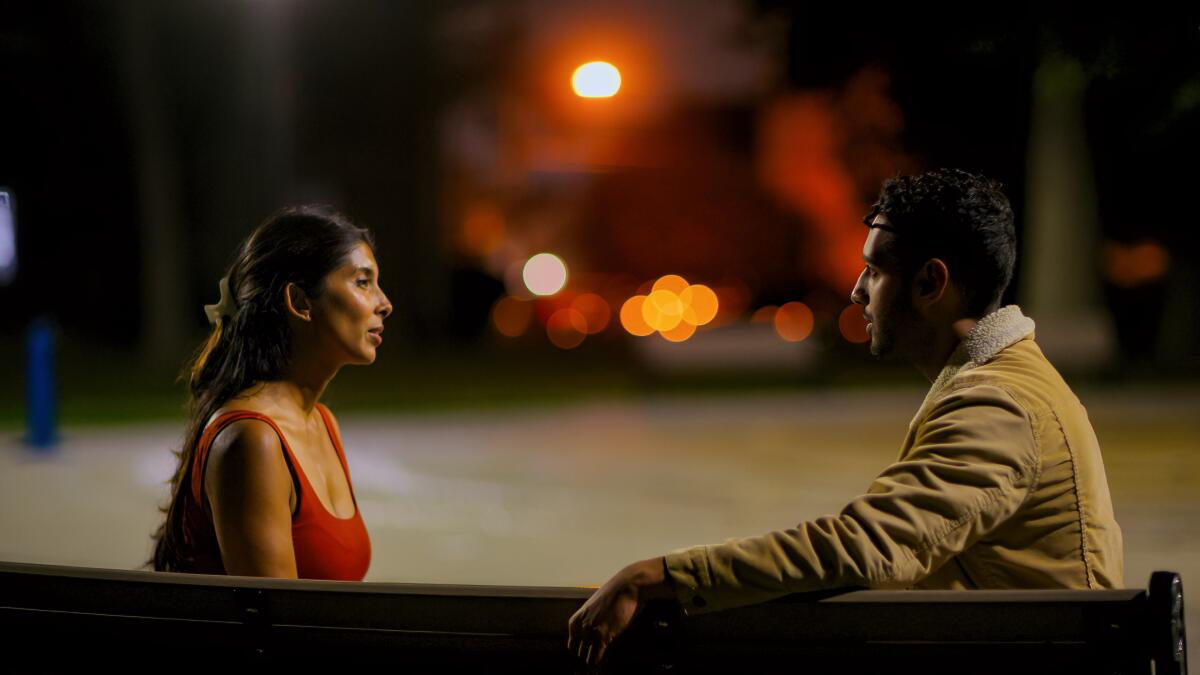 A woman and man sit facing each other and talking at night.