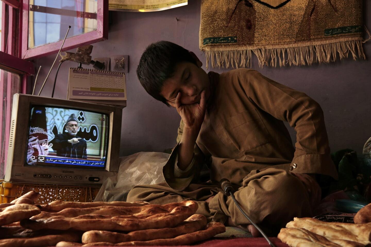 Sami Rahimi, 13, rests his head momentarily as a speech by Afghan President Hamid Karzai airs on a television in the Kabul bakery where he works. He begins his day before dawn.
