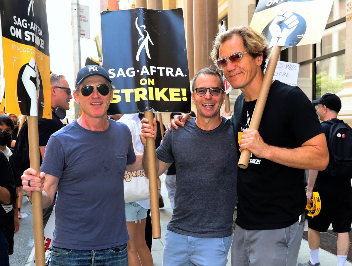 Three actors in dark T-shirts carrying picket signs