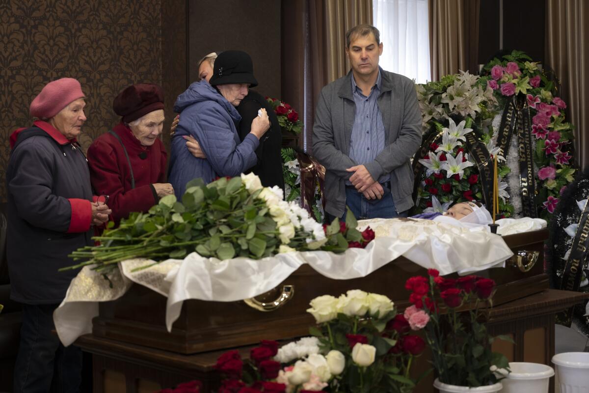 A man and several women standing over a flower-draped coffin.