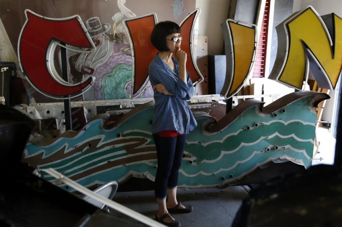 Kim Koga, director of the Museum of Neon Art, with Grauman's Chinese Theatre neon sign that is being stored in a warehouse in Pomona for restoration. MONA once located in downtown Los Angeles, is 18 months away from re-opening in Glendale.